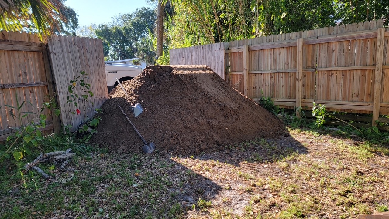 Large pile of fill dirt delivered to a fenced backyard for grading
